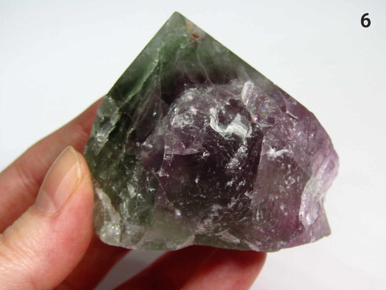 May include: A green and purple fluorite crystal with a pointed top and a rough, natural texture.