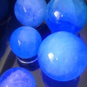 May include: Several blue crystal spheres of varying sizes are arranged on a reflective surface. The spheres have a translucent quality, with internal patterns and a glowing appearance. The color is a vibrant, saturated blue.