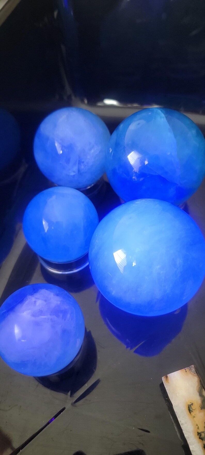 May include: Several blue crystal spheres of varying sizes are arranged on a reflective surface. The spheres have a translucent quality, with internal patterns and a glowing appearance. The color is a vibrant, saturated blue.
