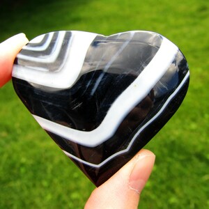 May include: A polished heart-shaped stone featuring alternating bands of deep black and bright white. The surface is smooth and reflective, displaying a distinct layered pattern throughout the entire object. The number 4 is visible in the corner.