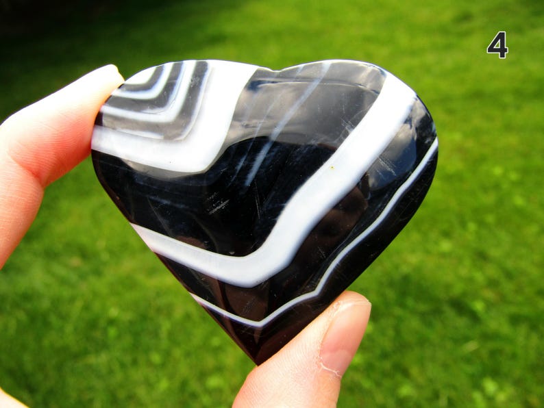 May include: A polished heart-shaped stone featuring alternating bands of deep black and bright white. The surface is smooth and reflective, displaying a distinct layered pattern throughout the entire object. The number 4 is visible in the corner.