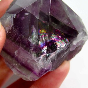 May include: A purple fluorite crystal with iridescent rainbow inclusions. The crystal is a double terminated point with a natural, rough surface.