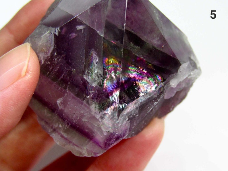 May include: A purple fluorite crystal with iridescent rainbow inclusions. The crystal is a double terminated point with a natural, rough surface.