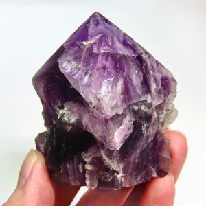 May include: A large, purple amethyst crystal with a pointed top and a rough, textured surface.