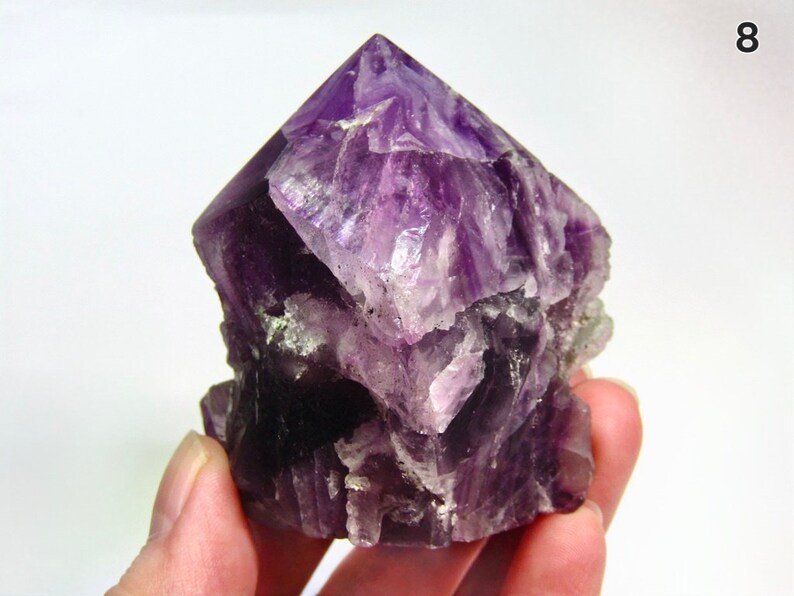 May include: A large, purple amethyst crystal with a pointed top and a rough, textured surface.