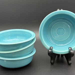May include: A set of turquoise ceramic bowls. One bowl is displayed on a black stand, while the others are stacked. The bowls have a circular design with concentric rings in the center and a ribbed texture.
