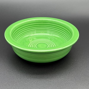 May include: A bright lime green ceramic bowl featuring a series of concentric circular ridges along the interior base and sides, with a smooth, wide, flat rim extending outward from the top edge of the bowl, creating a distinct tiered profile.