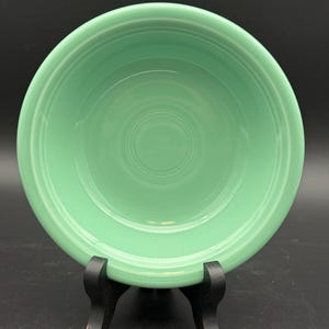 May include: A round, light green ceramic bowl featuring a smooth, glossy finish and concentric circular ridges embossed along the interior base and rim, providing a simple, functional design for serving food or displaying small items.