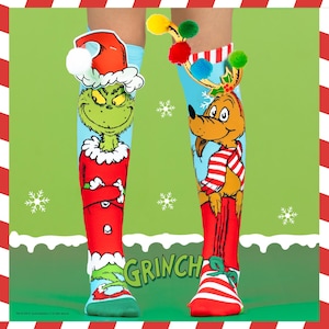 May include: A pair of knee-high socks featuring the Grinch and Max characters from the Dr. Seuss story. The Grinch sock has a red Santa hat and the word "Grinch" in green. The Max sock has reindeer antlers and a red and white striped scarf.