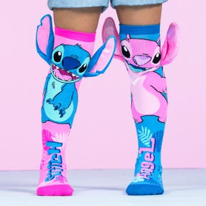 May include: A pair of knee-high socks featuring the characters Stitch and Angel from the Disney movie Lilo & Stitch. One sock is blue with Stitch, the other is pink with Angel. The word "Stitch" and "Angel" are printed on the socks.