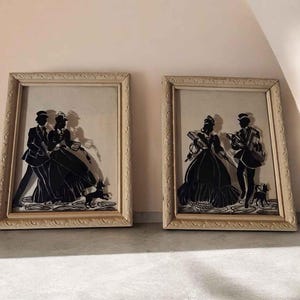 Peut inclure: Deux cadres muraux rectangulaires présentant des silhouettes en papier noir de couples en vêtements d'époque avec de petits chiens. Les cadres sont beige clair avec un motif sculpté texturé. Chaque silhouette représente des personnages marchant.