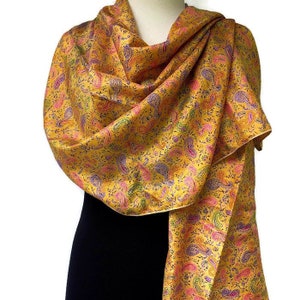 Può includere: Una sciarpa di seta gialla con un motivo paisley in tonalità di rosa, verde e viola. La sciarpa è piegata e drappeggiata su un manichino.