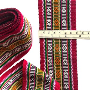 May include: Red, white, green, black and orange woven trim with a geometric pattern. The trim is 2 inches wide and is measured with a ruler.