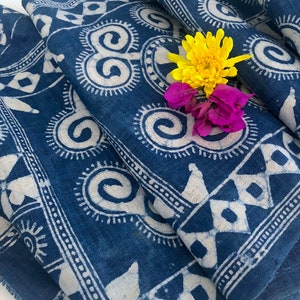 May include: A blue fabric with a white geometric pattern. The fabric is folded and has a yellow and purple flower on top.