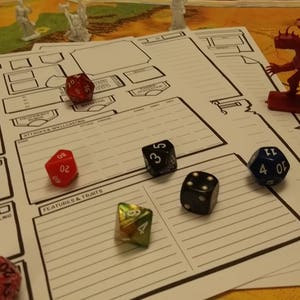 May include: A tabletop role-playing game setup with character sheets, dice, and miniature figurines. The dice are various colors, including red, black, and blue. A red dragon figurine and white figurines are also present.