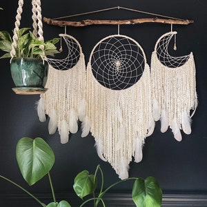 May include: Three white dreamcatchers with feathers hanging from a branch. The dreamcatchers are arranged in a crescent shape. The dreamcatchers are made with white yarn and feathers.