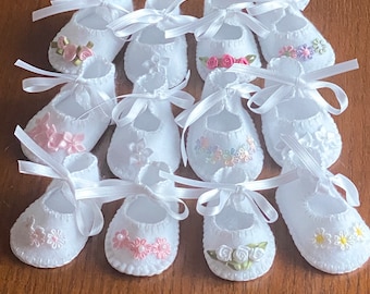 May include: Twelve pairs of white baby booties with satin ribbon ties and embroidered floral designs. The booties are made of soft fabric and are perfect for a newborn baby.