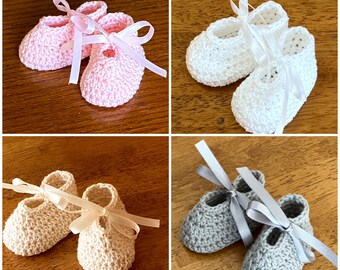 May include: Three pairs of crocheted baby booties with satin ribbon ties. The booties are in pink, white, and beige.