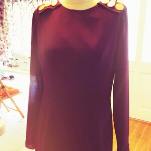 May include: A long-sleeved, burgundy dress with gold buttons on the shoulders.