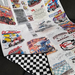 May include: A white quilt with a checkered pattern on the back. The front is made of various patches of fabric with images of race cars and the text "Deming Speedway" and "Clay Cup Nationals".