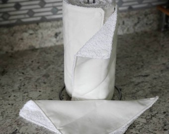 May include: White reusable paper towels on a metal stand. The towels are made of a soft, absorbent fabric and are designed to be washable and reusable. The towels are folded and rolled up, and they are ready to be used.