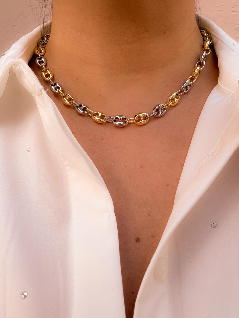 May include: A two-tone chain necklace with alternating gold and silver links. The necklace is a chunky style, resting on a white collared shirt. The gold and silver tones create a striking contrast, making it a versatile accessory.