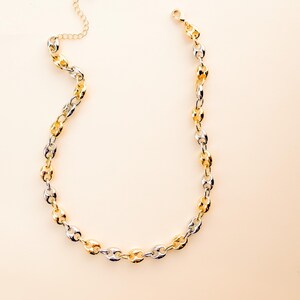May include: A gold and silver-toned chain necklace. The necklace features a series of oval-shaped links, alternating between gold and silver. The necklace has a lobster clasp closure and an adjustable chain.