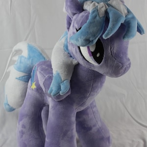 May include: A plush toy of a purple pony with a blue mane and tail. The pony has a star on its flank and a white mane and tail.