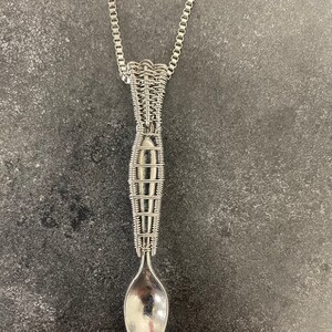 May include: A silver spoon necklace with a wire-wrapped design. The spoon is suspended from a silver chain.