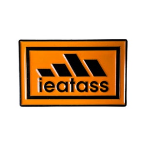 May include: Orange and black enamel pin with a parody of the Adidas logo and the text "ieatass".