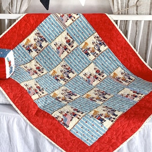 Op de afbeelding: Een rood, wit en blauw babydeken met een patriottisch thema. Het deken heeft een herhalend patroon van marsbandfiguren die instrumenten bespelen. Het deken is gemaakt van zachte, comfortabele stof en is perfect voor een kinderkamer of speelkamer.