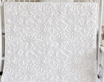 Könnte beinhalten: Eine weiße Babydecke mit einem durchgehenden Steppmuster aus stilisierten Blumen und geschwungenen Ranken. Der Stoff hat eine gleichmäßige matte Textur mit sichtbaren Nähten, die einen erhabenen, geprägten Effekt auf der gesamten Oberfläche erzeugen.