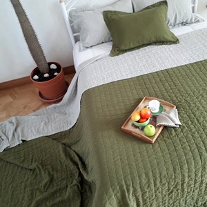 Puede incluir: Una cama con ropa de cama verde oliva y gris. La cama tiene una colcha verde oliva acolchada y una almohada a juego. Una bandeja de madera con fruta y una taza de t&eacute; est&aacute; sobre la cama. Un cactus en maceta est&aacute; al lado de la cama.