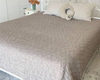 May include: A bed with a white metal frame and a beige quilted bedspread. Two beige pillows and a decorative pillow are on the bed. A white nightstand with a vase of dried flowers is next to the bed.