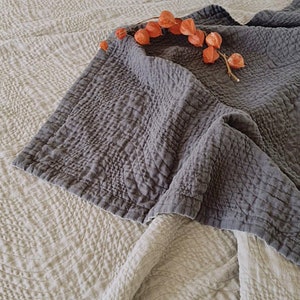May include: A gray quilted throw blanket with a textured pattern. The blanket is folded and draped over a white textured blanket.