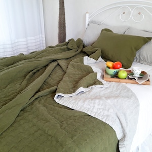 Puede incluir: Una cama con cabecero de metal blanco est&aacute; cubierta con un edred&oacute;n y almohadas verdes. Una bandeja de madera contiene un cuenco de fruta y una taza de t&eacute;. El edred&oacute;n es verde oliva por un lado y gris claro por el otro.