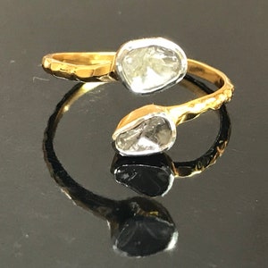 May include: A gold ring with two clear, faceted gemstones. The ring is twisted and has a hammered texture.