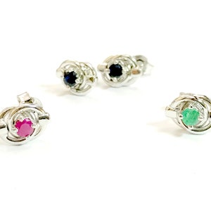 May include: Three pairs of silver stud earrings with different colored gemstones. The first pair has blue gemstones, the second pair has red gemstones, and the third pair has green gemstones.