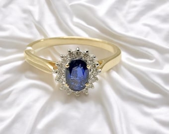 May include: A gold ring with a large oval blue sapphire surrounded by a halo of smaller diamonds.