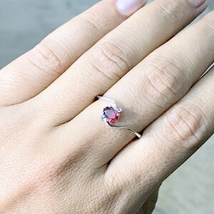 May include: A silver ring with a red oval gemstone and smaller clear gemstones on the band.