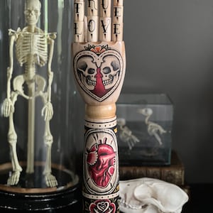 Wooden arm and hand with a skeleton couple and anatomical heart tattoo design