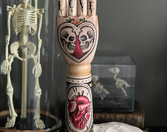 Hölzerner Arm und Hand mit einem Skelettpaar und anatomischem Herz-Tattoo-Design