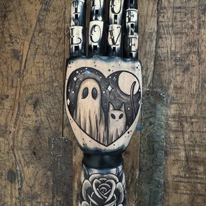 Zwarte houten hand met een geest en een kat- en roos-tatoeage