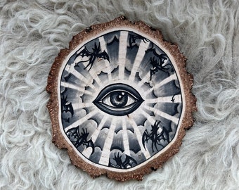 Wood slice with an original drawing of an all seeing eye tattoo design.