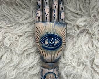 Main bleue en bois avec un dessin de tatouage d'oeil et de crâne ailé