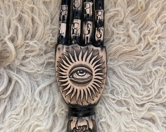 Schwarze Holzhand mit einem alles sehenden Auge und geflügeltem Totenkopf Tattoo Design