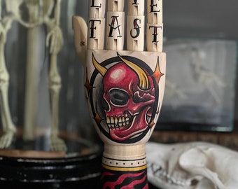 Hölzerne Hand mit gehörntem Totenkopf und Flammen-Tattoo-Design