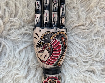 Black wooden hand with a snake and rose tattoo design