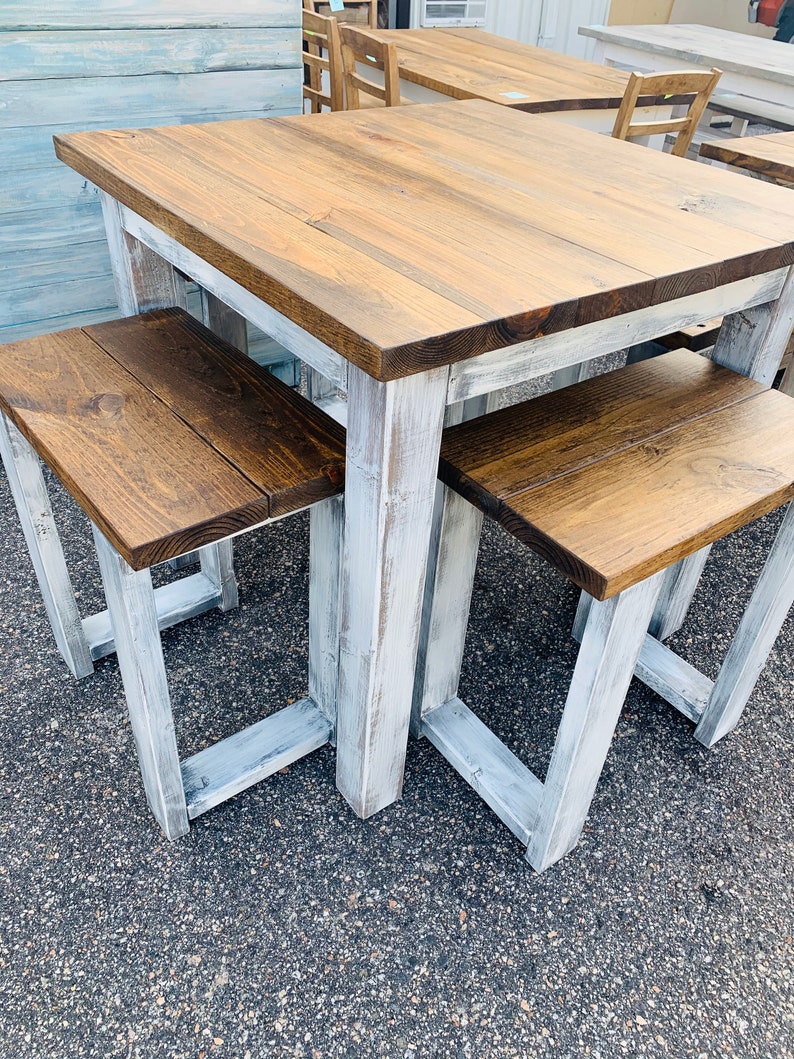 K&ouml;nnte beinhalten: Ein quadratischer Holztisch mit dunkelbraun gebeizter Tischplatte und einem wei&szlig; gestrichenen Gestell im Used-Look, dazu zwei passende rechteckige B&auml;nke mit dunkelbraunen Sitzfl&auml;chen und wei&szlig; lackierten Beinen in robuster Blockbauweise.