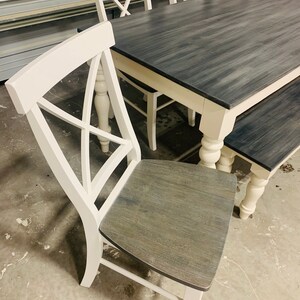 K&ouml;nnte beinhalten: Ein Esszimmerset bestehend aus einem rechteckigen Tisch und St&uuml;hlen mit wei&szlig;en Rahmen und dunkelgrau gebeizten Holzoberfl&auml;chen. Die St&uuml;hle haben ein X-f&ouml;rmiges R&uuml;ckendesign und die Tisch- sowie Bankbeine sind gedrechselt.